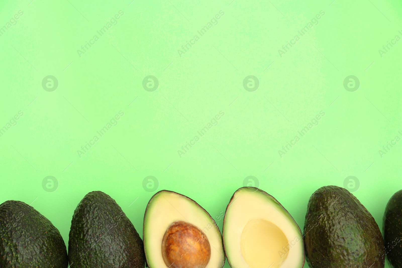 Photo of Tasty whole and cut avocados on light green background, flat lay. Space for text