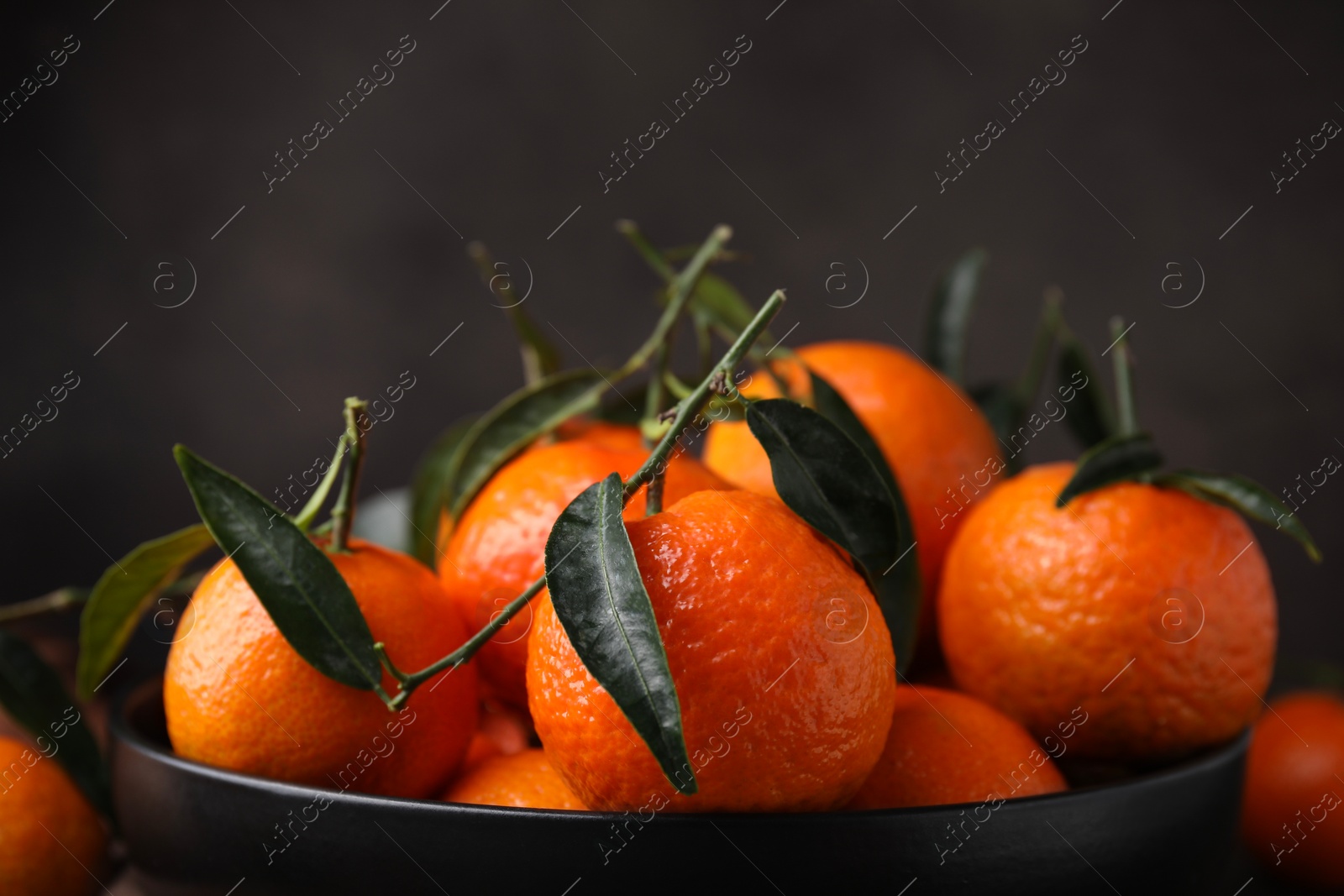 Photo of Fresh ripe tangerines with green leaves in bowl on table, closeup