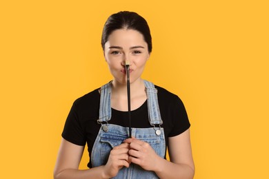 Woman with paintbrush on yellow background. Young artist