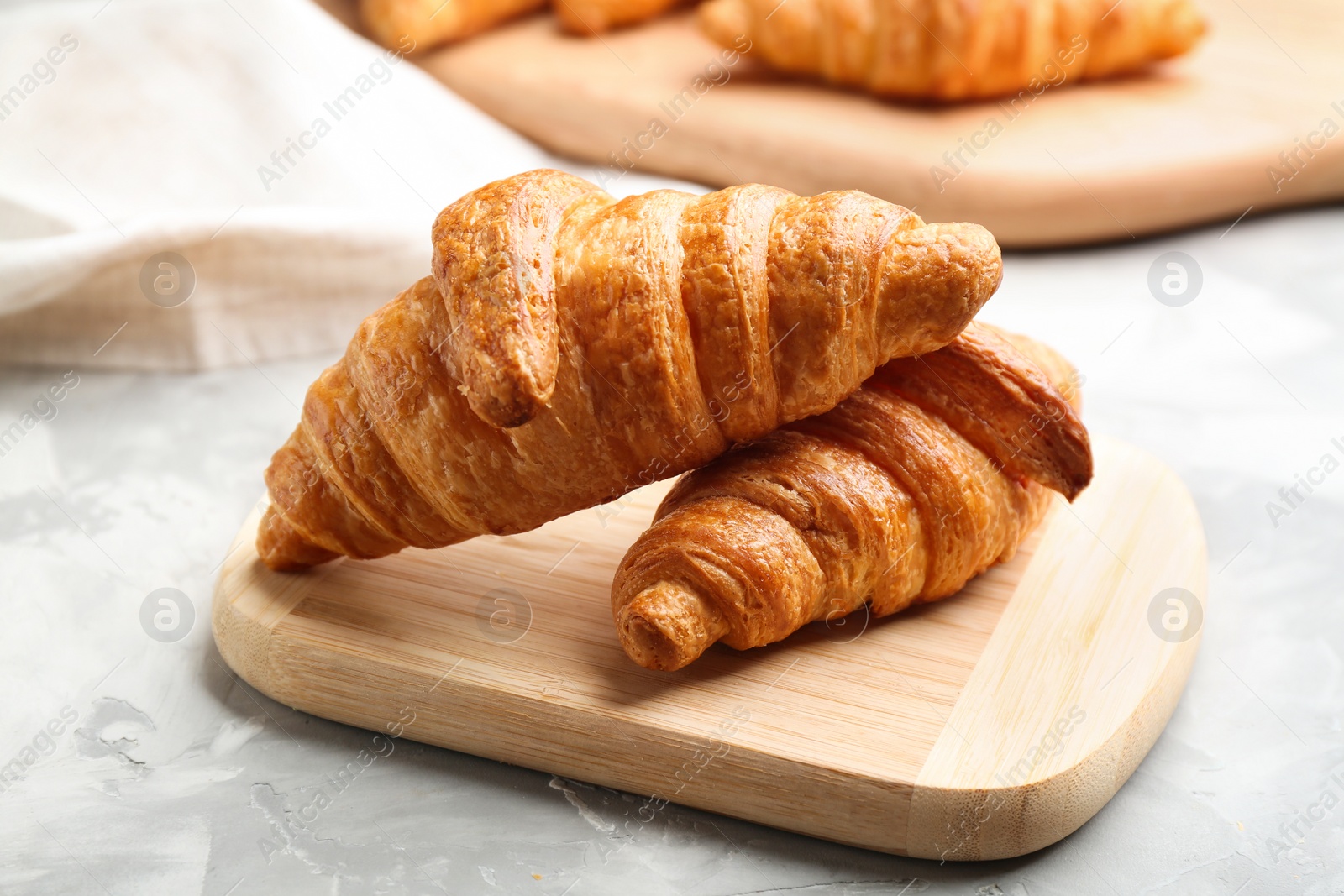 Photo of Wooden board with fresh croissants on grey table, closeup. French pastry