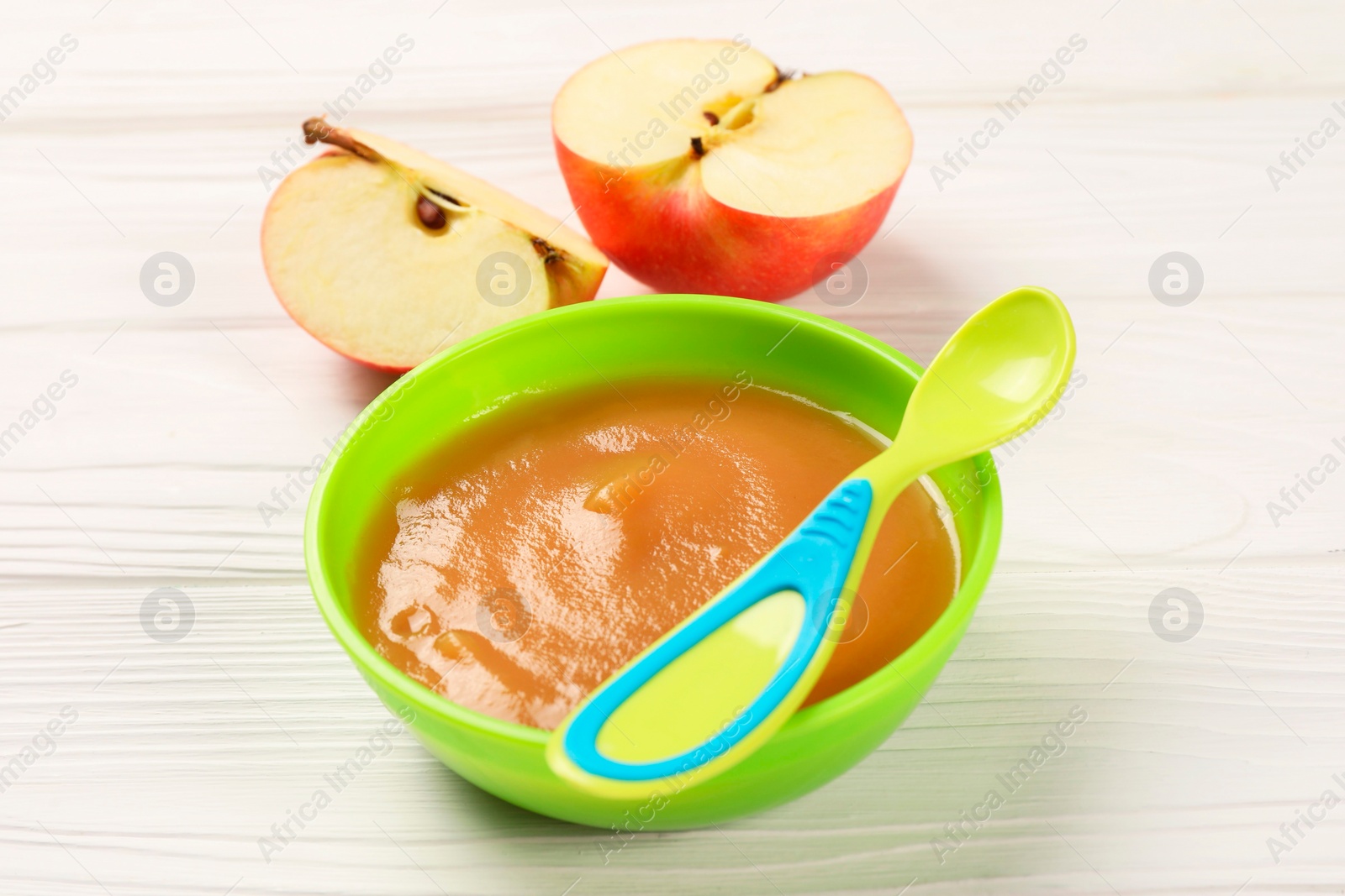 Photo of Baby food. Puree of apples in bowl and spoon on white wooden table