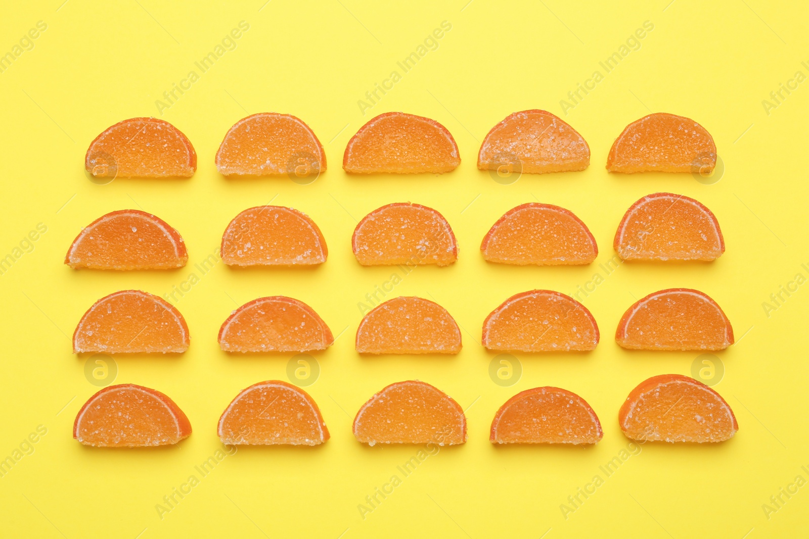 Photo of Delicious orange marmalade candies on yellow background, flat lay