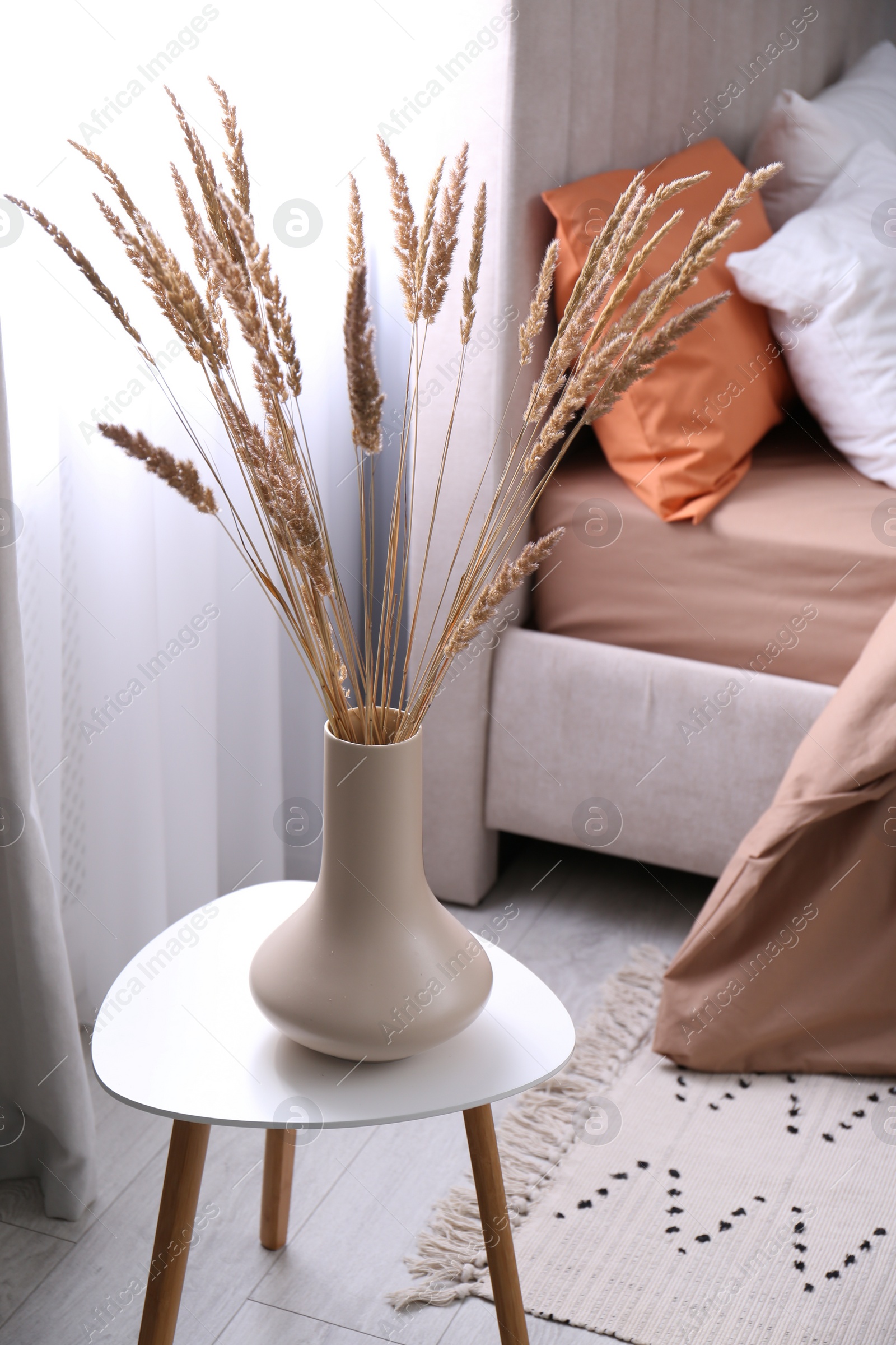 Photo of Vase with decorative dried plants on table in bedroom. Interior design