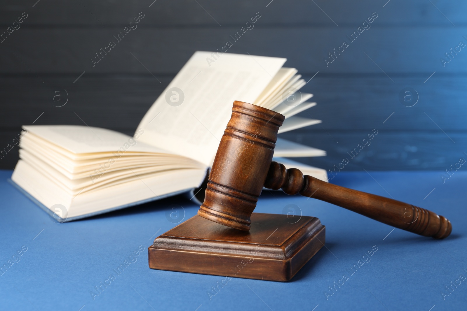 Photo of Wooden gavel, sound block and book on blue table, closeup