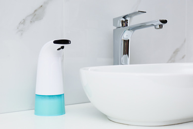 Modern automatic soap dispenser near sink in bathroom, closeup