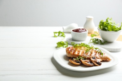 Photo of Tasty grilled chicken fillet with mushrooms and arugula on white wooden table. Space for text