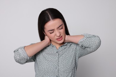 Photo of Young woman suffering from pain in neck on light grey background. Arthritis symptoms