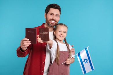 Photo of Immigration. Happy man with his daughter holding passports and flag of Israel on light blue background, space for text