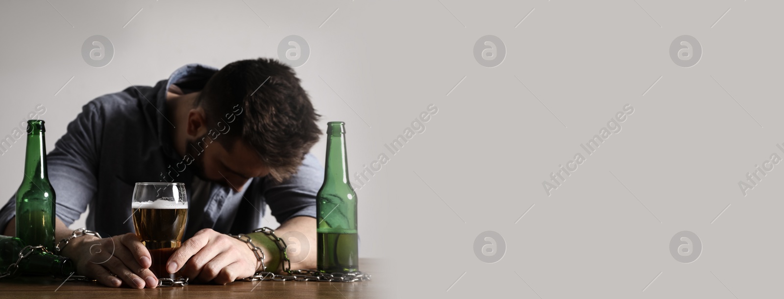 Image of Suffering from hangover. Man chained with glass of alcoholic drink at table against white background, space for text. Banner design