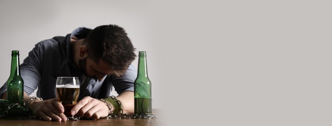 Suffering from hangover. Man chained with glass of alcoholic drink at table against white background, space for text. Banner design