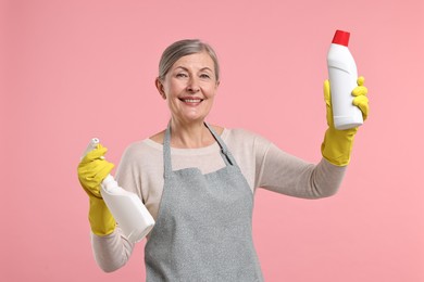 Happy housewife with bottles of detergent on pink background