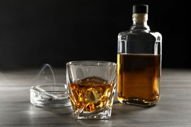 Photo of Alcohol addiction. Whiskey in glass, bottle, cigarettes and ashtray on wooden table
