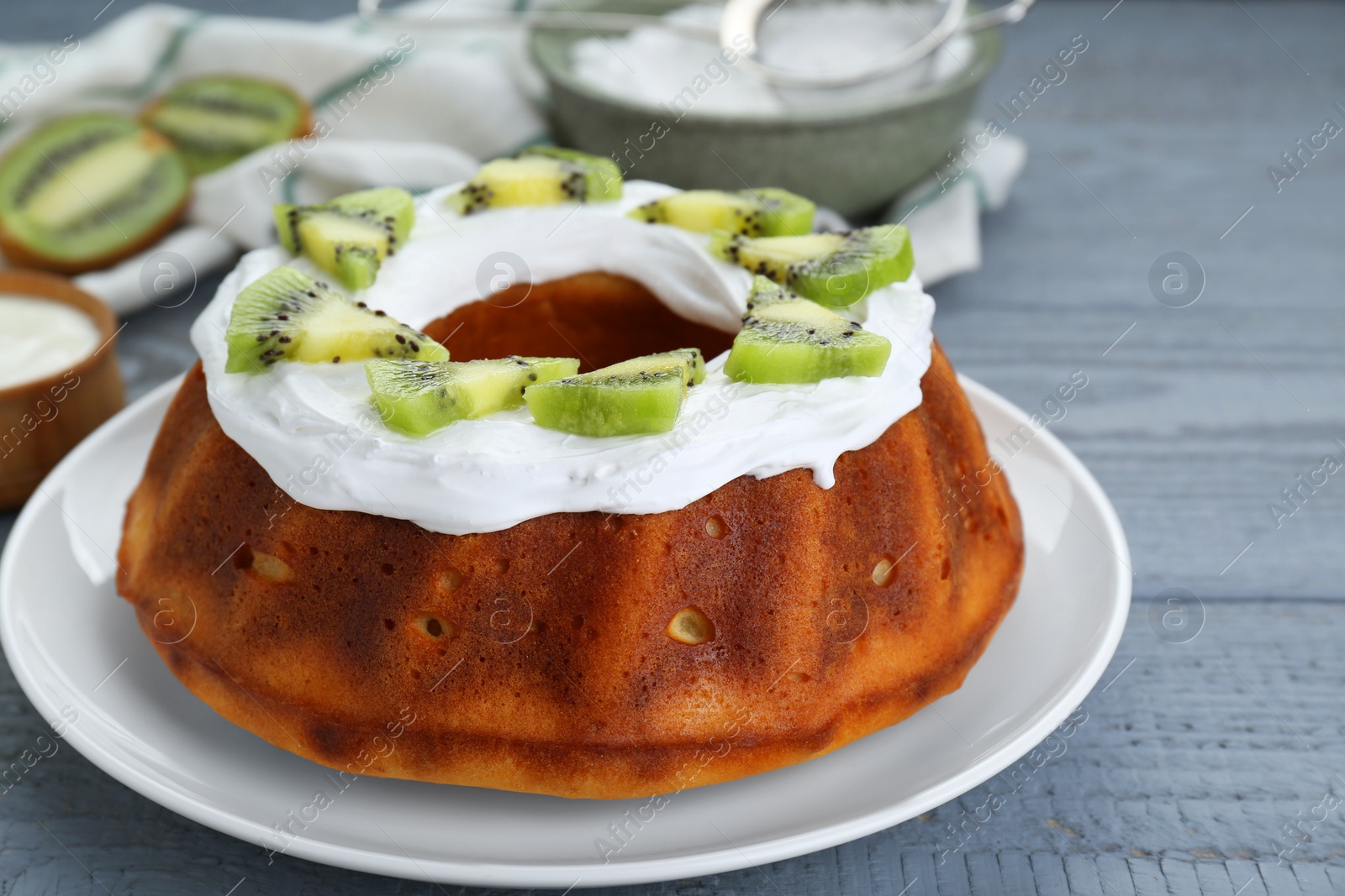 Photo of Homemade yogurt cake with kiwi and cream on grey wooden table, closeup