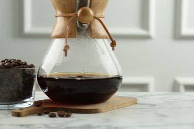 Photo of Glass chemex coffeemaker with coffee and beans on white marble table, closeup. Space for text