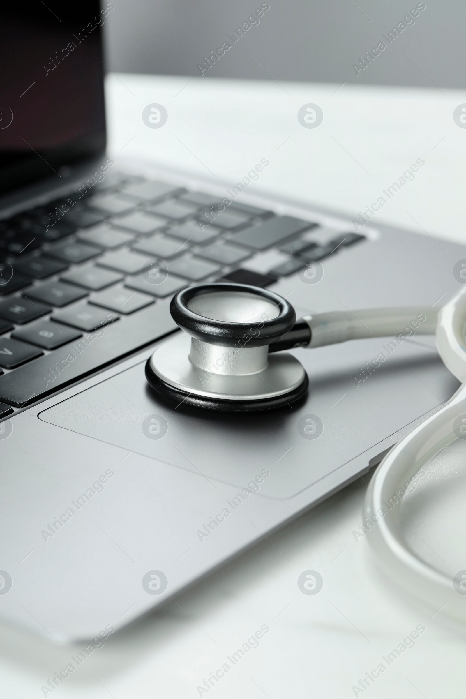 Photo of Modern laptop and stethoscope on white table, closeup