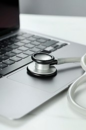 Modern laptop and stethoscope on white table, closeup