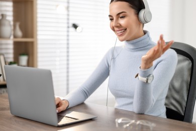Photo of Young woman in headphones using video chat during webinar at table in office