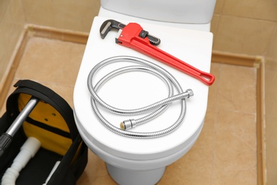 Photo of Pipe wrench and flexible hose on toilet seat lid indoors