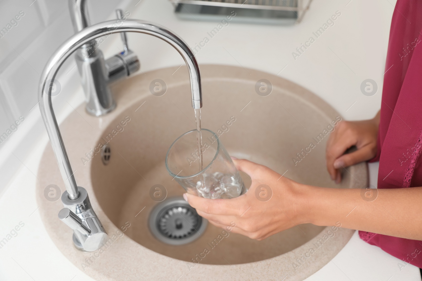 Photo of Woman pouring water into glass in kitchen, closeup