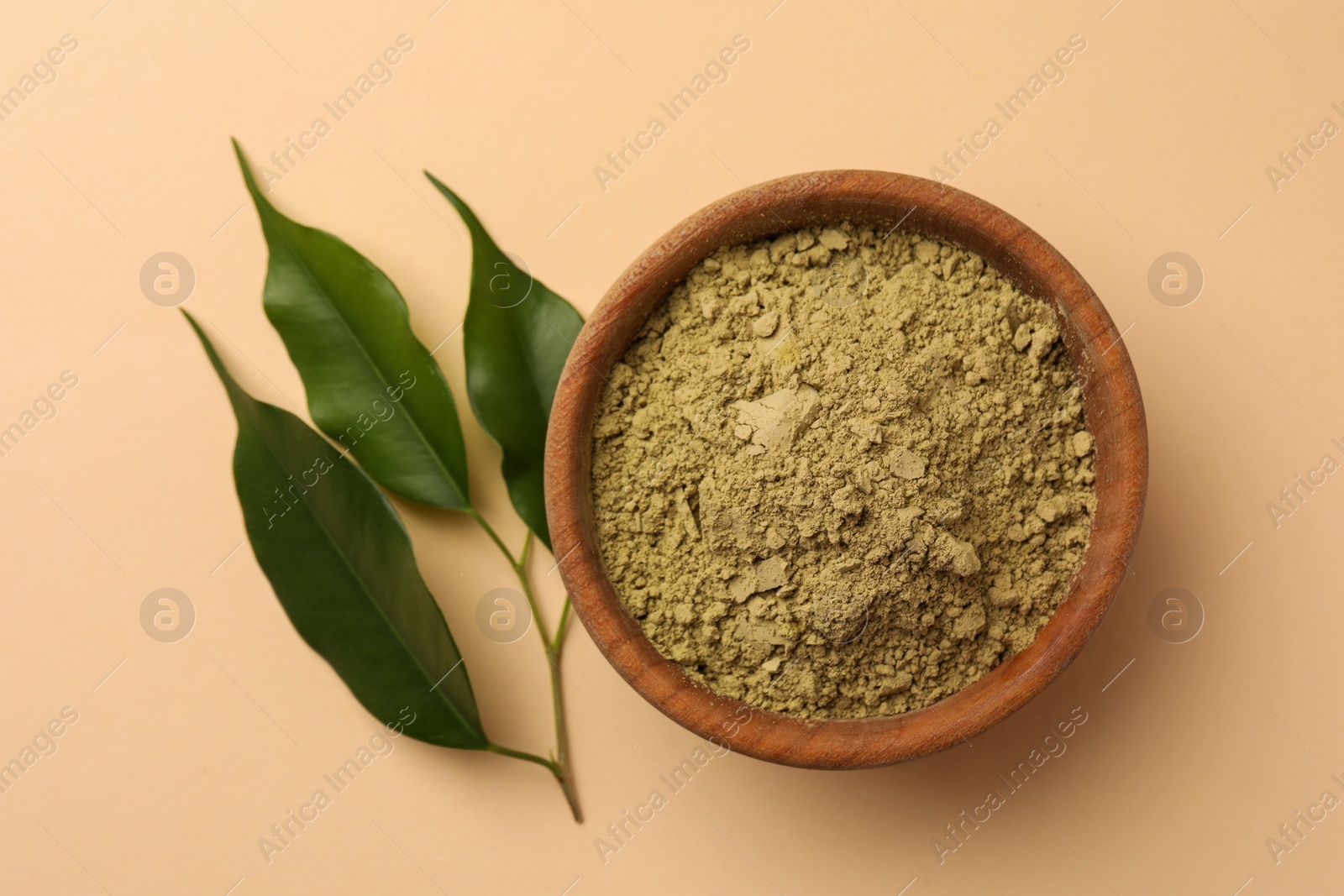Photo of Henna powder and green leaves on beige background, flat lay. Natural hair coloring