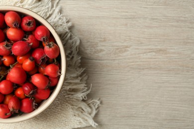 Ripe rose hip berries in bowl on wooden table, top view. Space for text