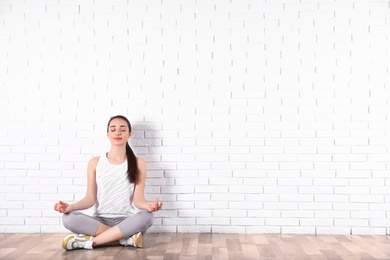 Photo of Young woman meditating on floor near brick wall, space for text. Zen concept