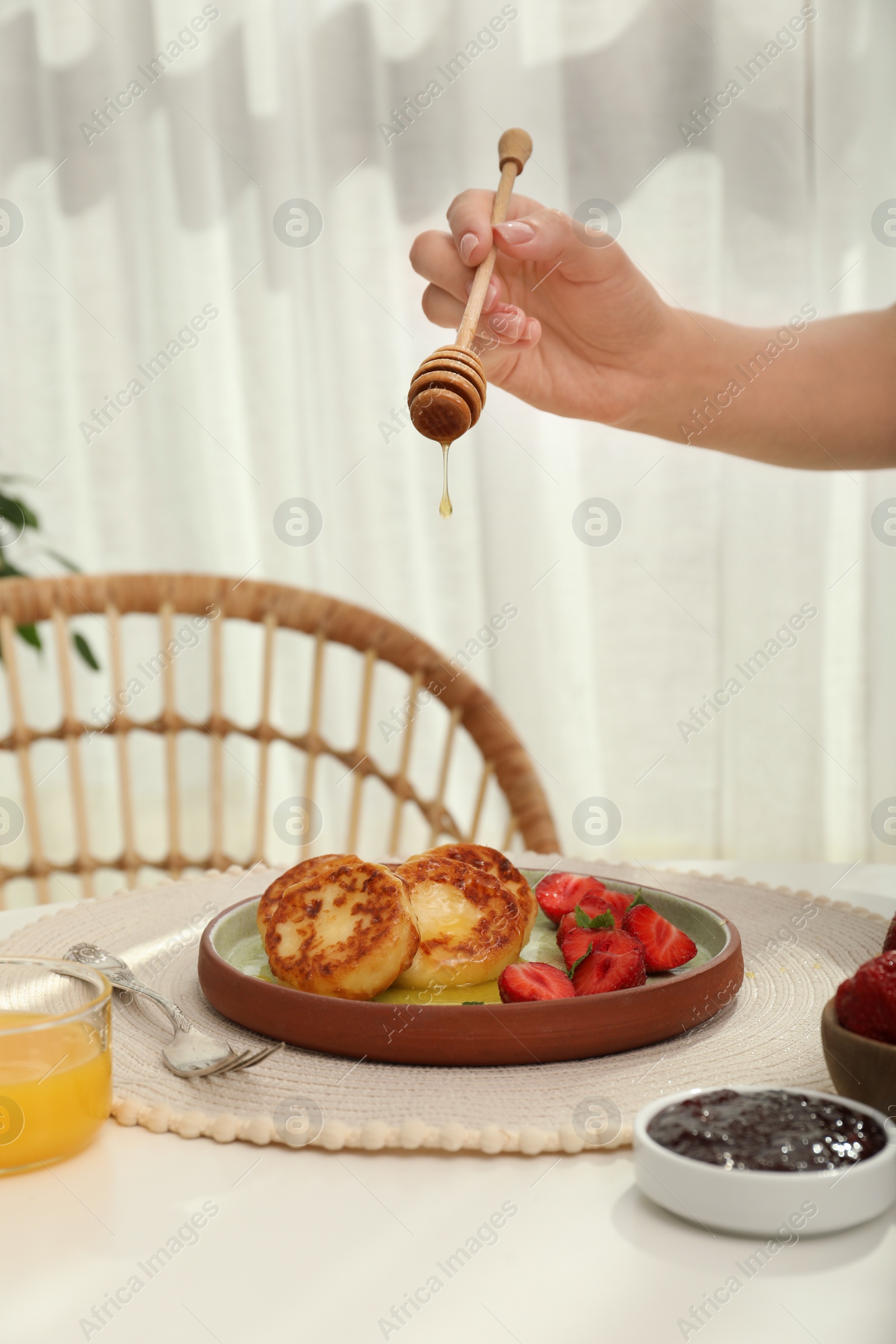 Photo of Woman pouring honey onto delicious cottage cheese pancakes at white table indoors, closeup