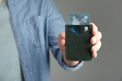 Man holding leather card holder with credit cards on grey background, closeup