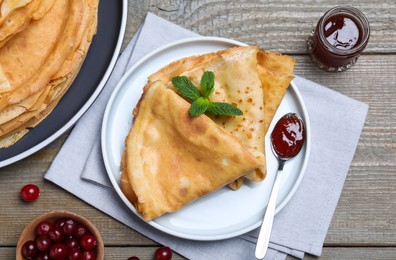 Photo of Delicious crepes served with mint, cranberries and jam on grey wooden table, flat lay