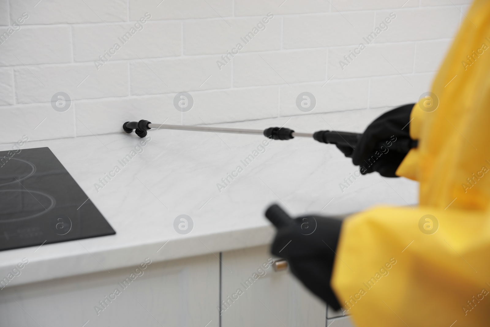 Photo of Pest control worker spraying pesticide on kitchen counter, closeup