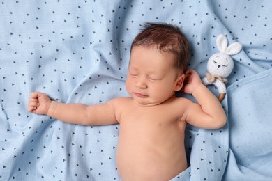 Cute newborn baby with toy bunny sleeping on bed, top view