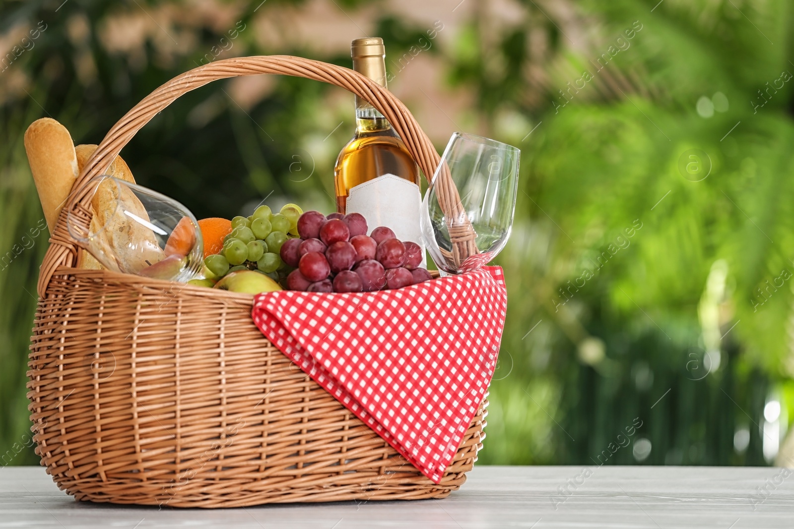 Photo of Picnic basket with products and wine on table against blurred background, space for text