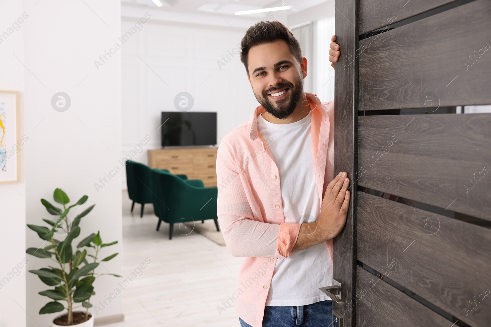 Photo of Happy man standing near door, space for text. Invitation to come indoors