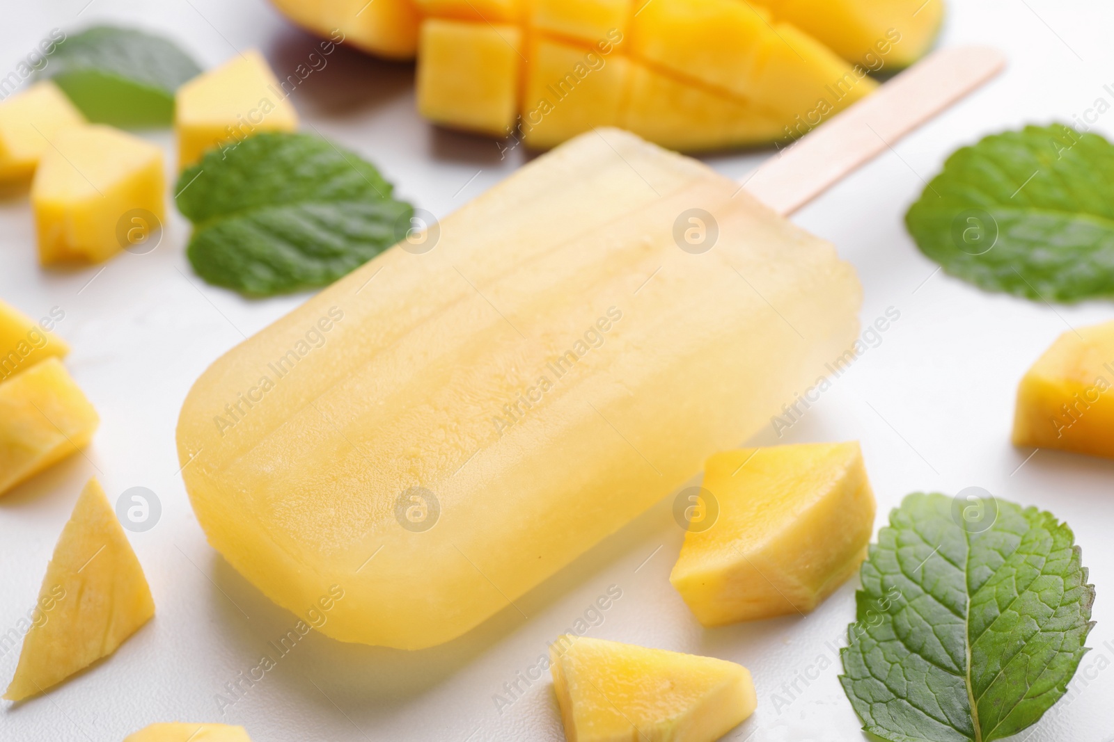 Photo of Tasty mango ice pop on white table, closeup. Fruit popsicle