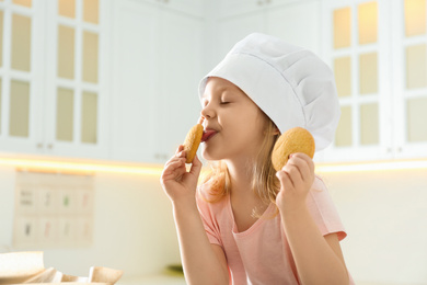 Little girl in chef hat eating cookies in kitchen