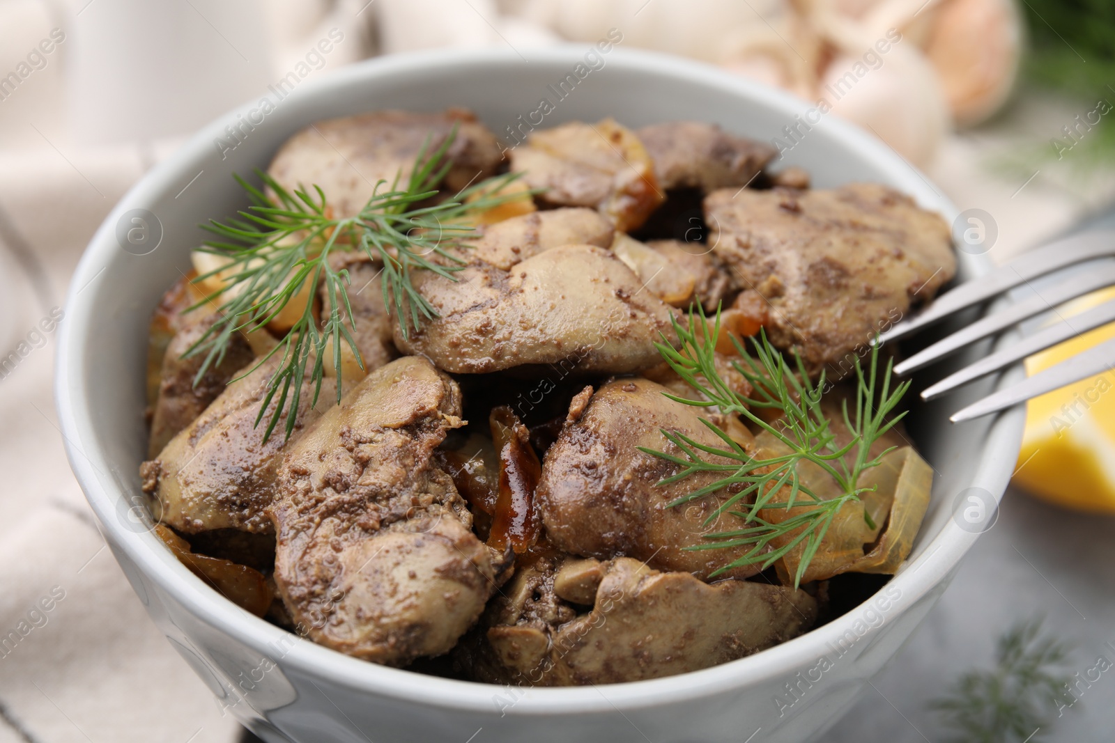 Photo of Tasty fried chicken liver with dill and fork on grey table, closeup