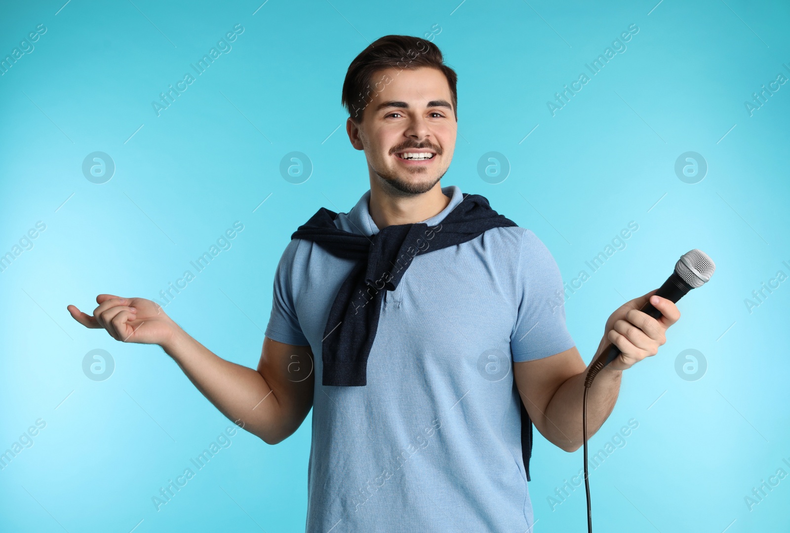 Photo of Young handsome man in casual clothes posing with microphone on color background