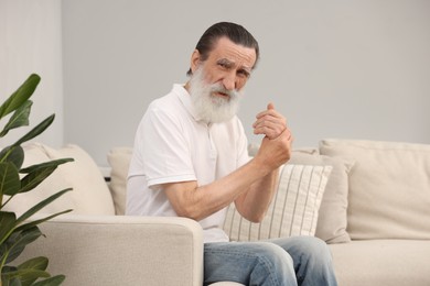 Photo of Senior man suffering from pain in hand on sofa at home. Rheumatism symptom