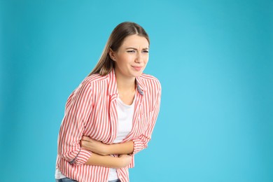 Photo of Woman suffering from stomach ache on light blue background, space for text. Food poisoning