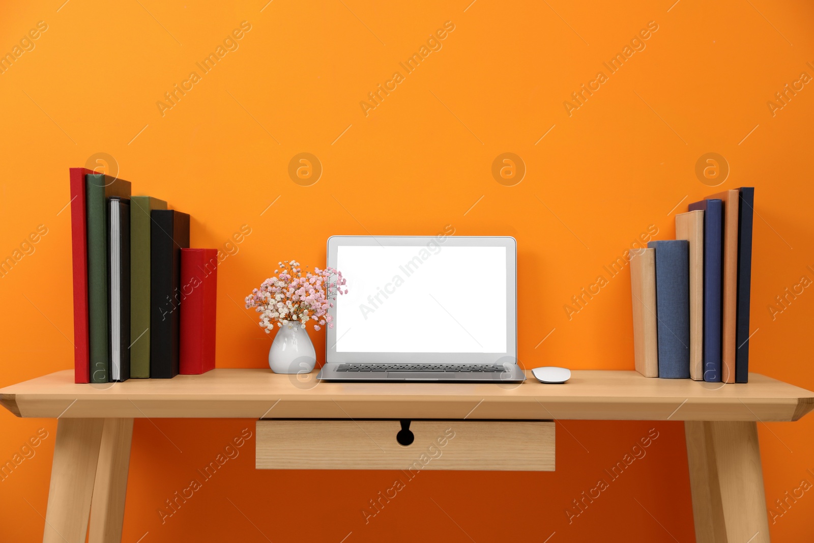 Photo of Hardcover books and laptop on wooden table near orange wall