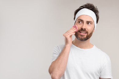 Photo of Man with headband washing his face using sponge on light grey background, space for text