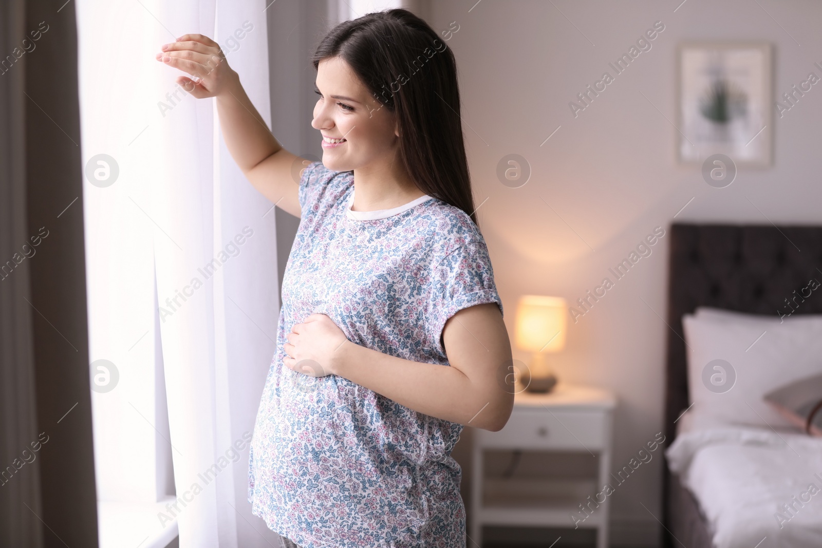 Photo of Young pregnant woman near window at home