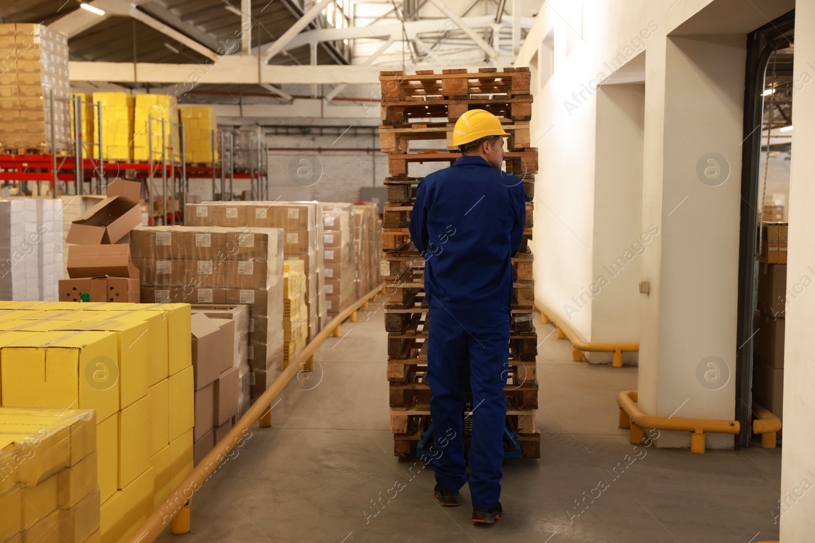 Image of Worker moving wooden pallets with manual forklift in warehouse, back view