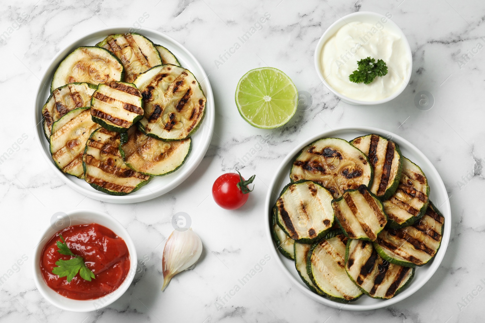 Photo of Grilled zucchini slices served with sauces on white marble table, flat lay