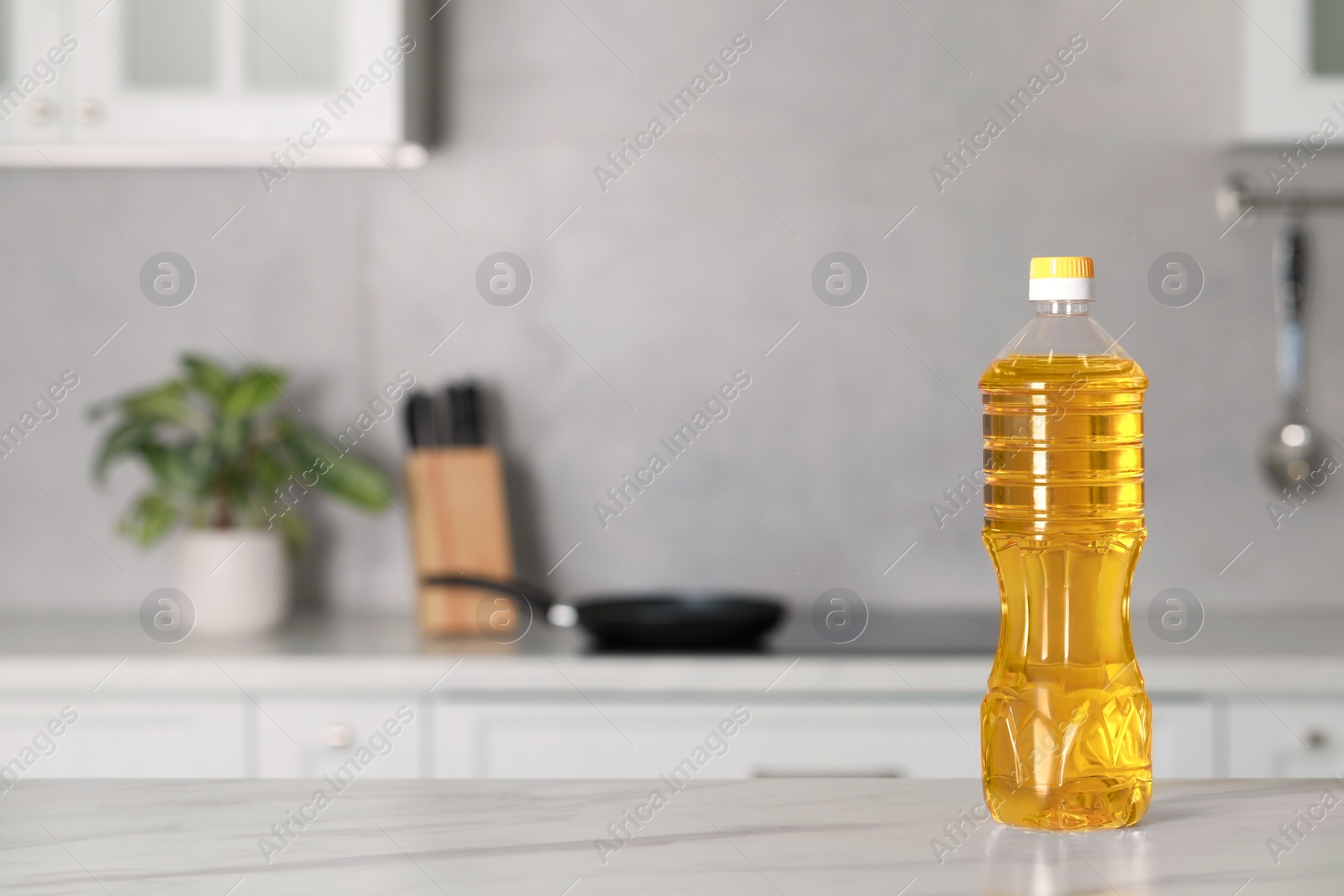 Photo of Bottle of cooking oil on white marble table in kitchen. Space for text