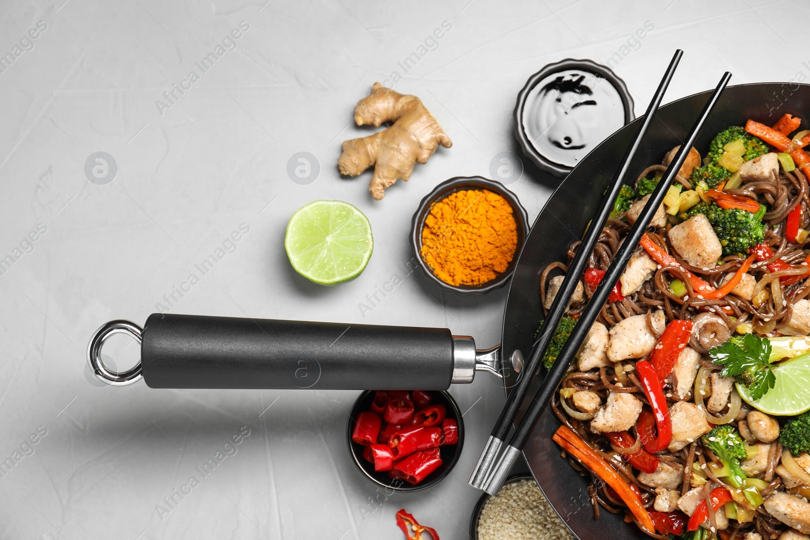 Photo of Stir-fry. Tasty noodles with meat in wok, chopsticks and ingredients on grey textured table, flat lay