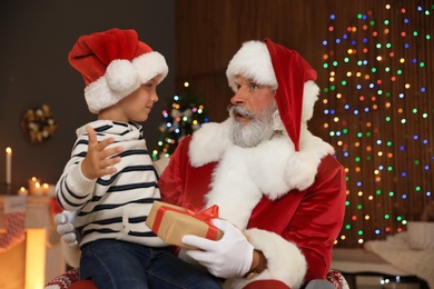 Photo of Little child with Santa Claus and Christmas gift at home