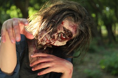 Photo of Scary zombie with bloody face outdoors, closeup. Halloween monster