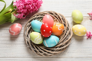 Photo of Flat lay composition of wicker nest with colorful painted Easter eggs and flower on table