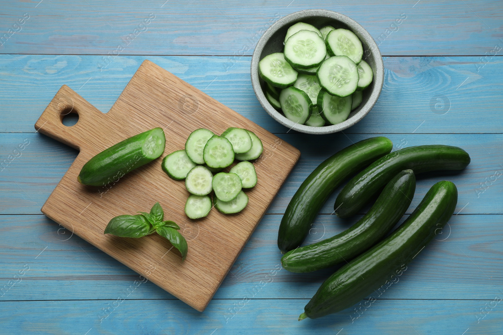 Photo of Fresh ripe cucumbers and basil on light blue wooden table, flat lay